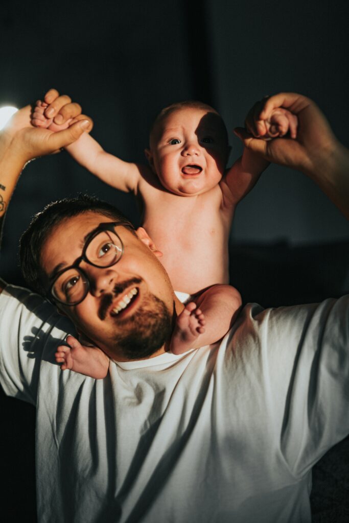 Pai sorrindo e brincando com o bebê durante a troca de fralda.