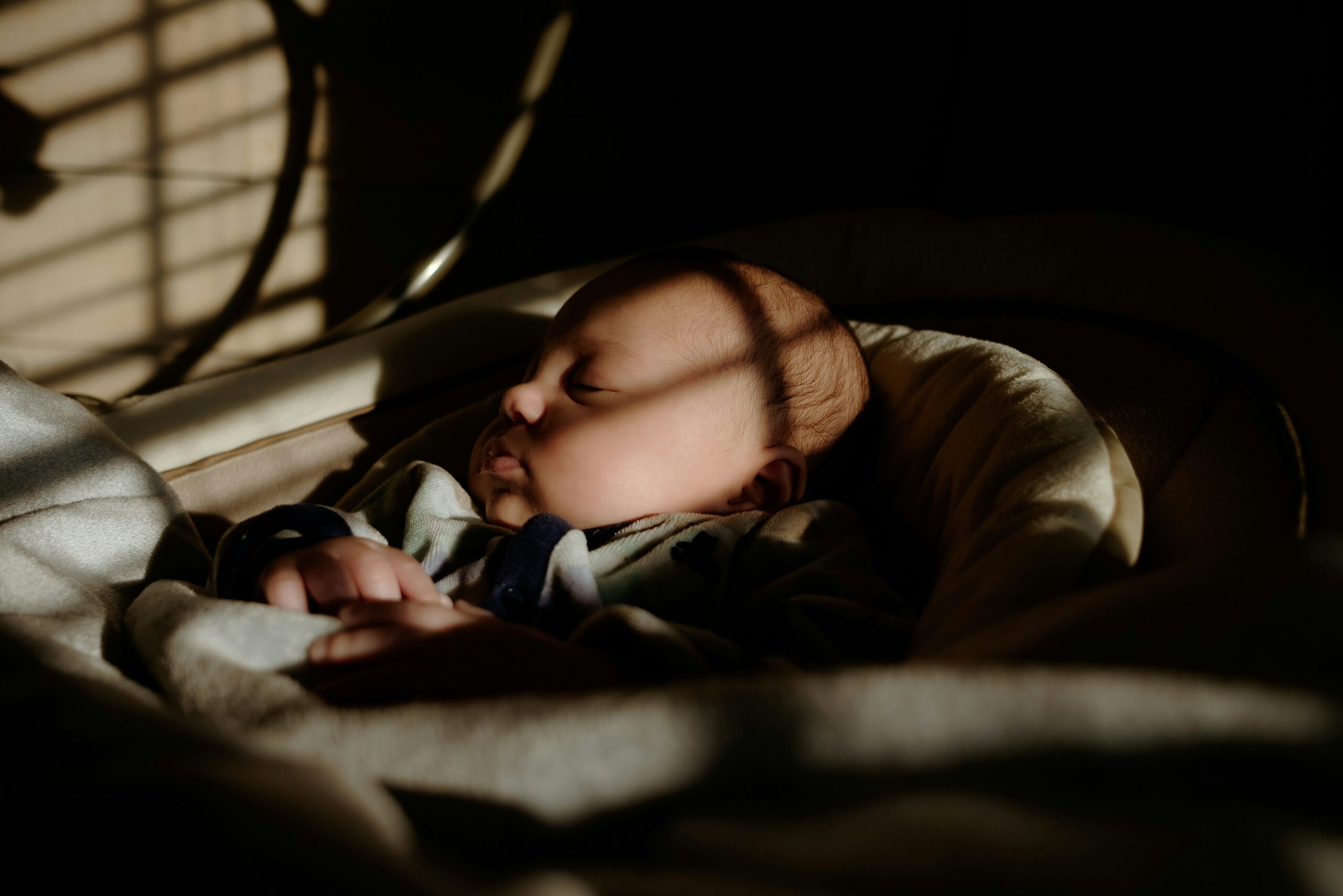 Um bebê recém-nascido dormindo durante o dia, com luz natural ao fundo
